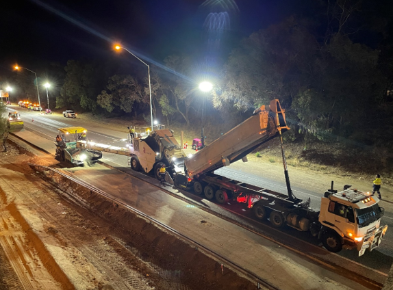 YongaCivil crew carrying out night road maintenance works under floodlights, with a road profiler and low-loader truck resurfacing a highway in Western Australia