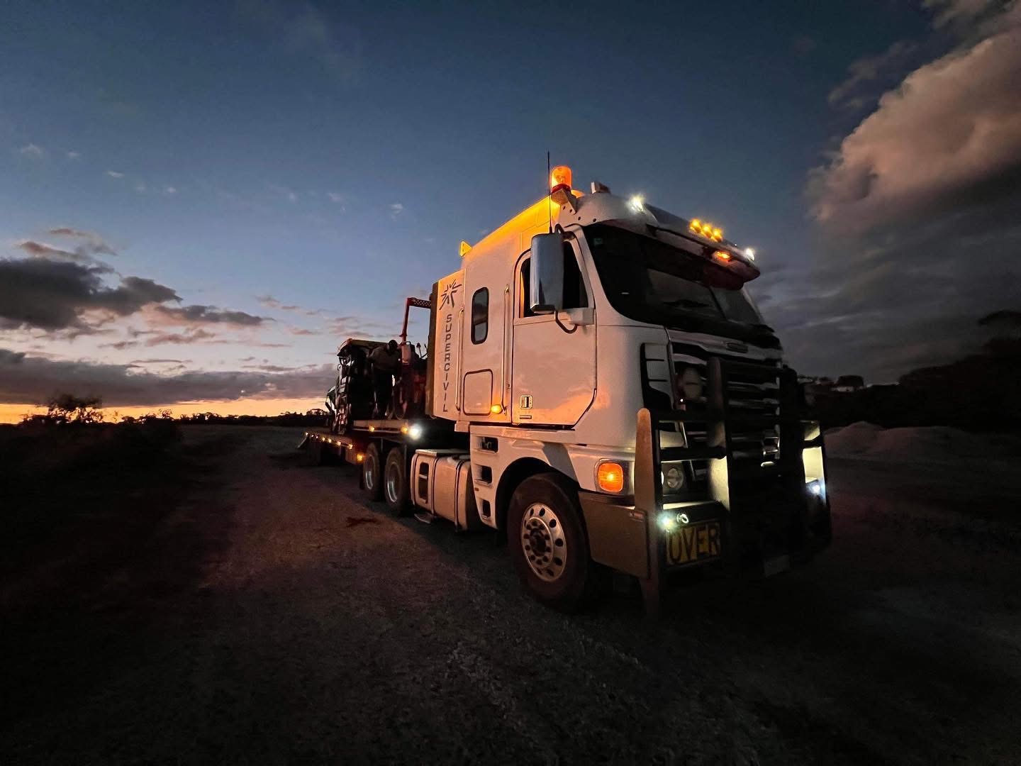 YongaCivil Freightliner prime mover hauling heavy plant on a low loader along a rural Western Australian haul road at dusk