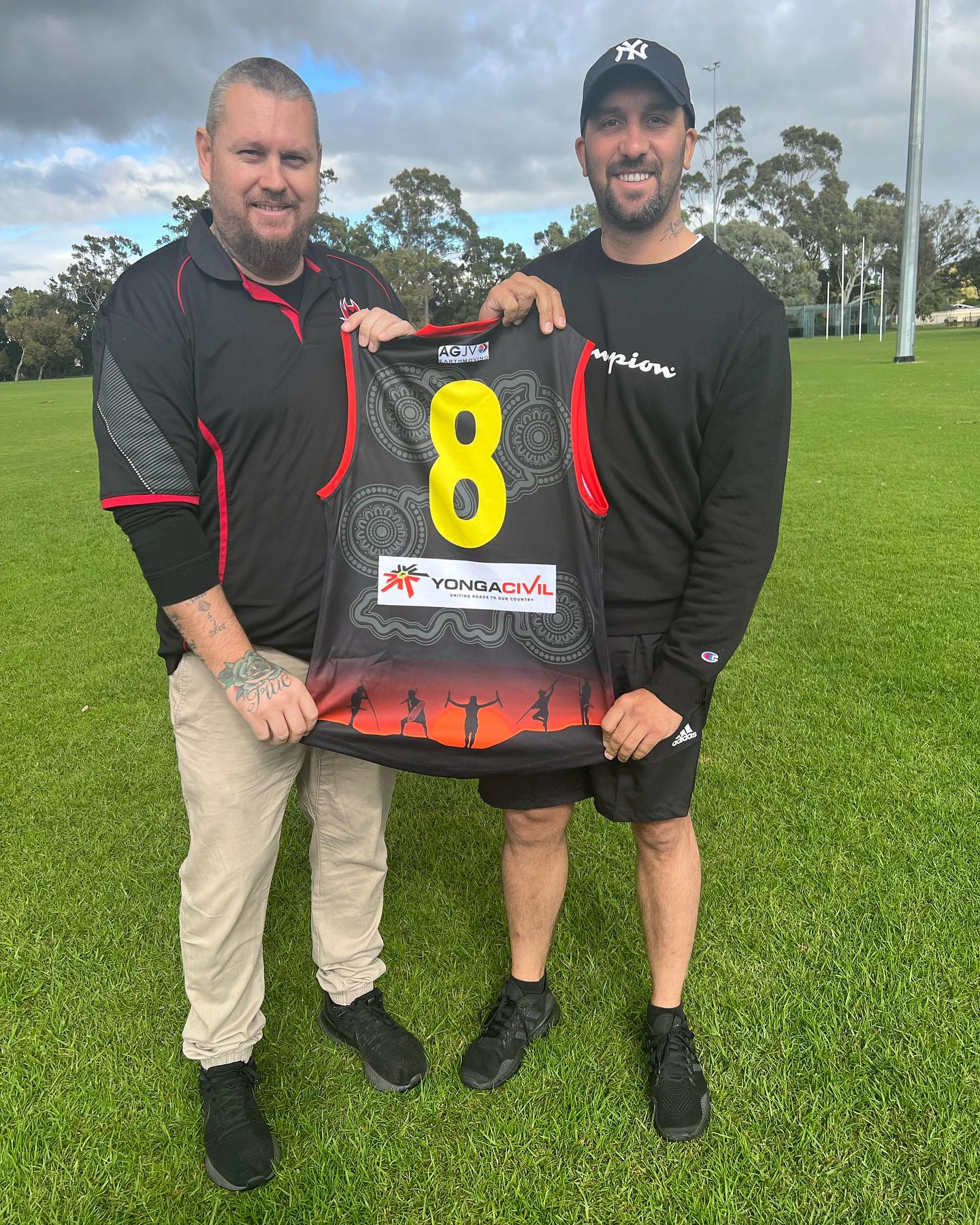 Two men on a football oval holding up a YongaCivil-sponsored Aboriginal-design football jersey