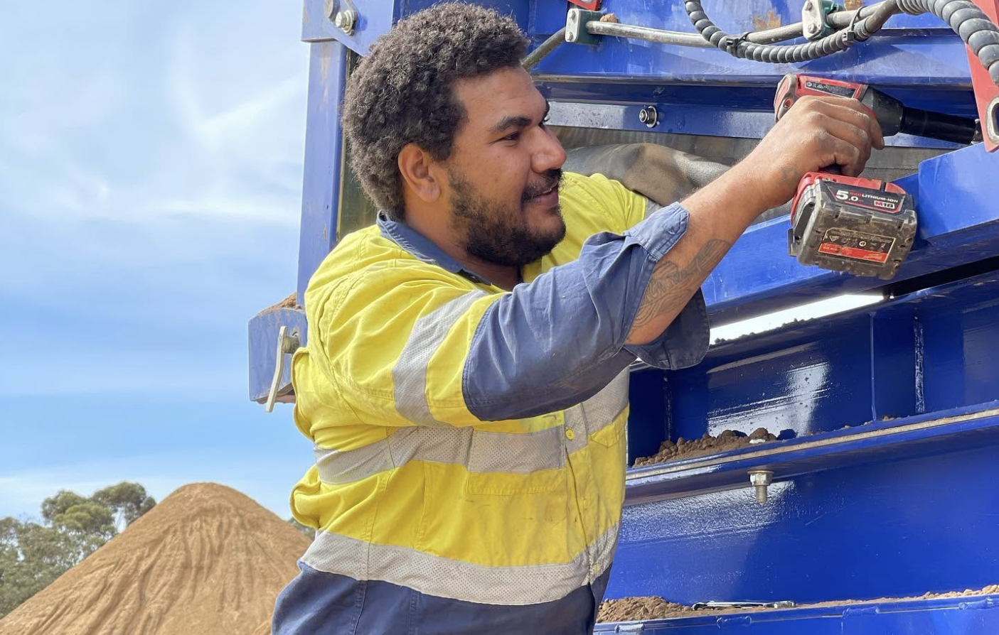 YongaCivil worker using an impact drill on a screening plant beside a sand stockpile