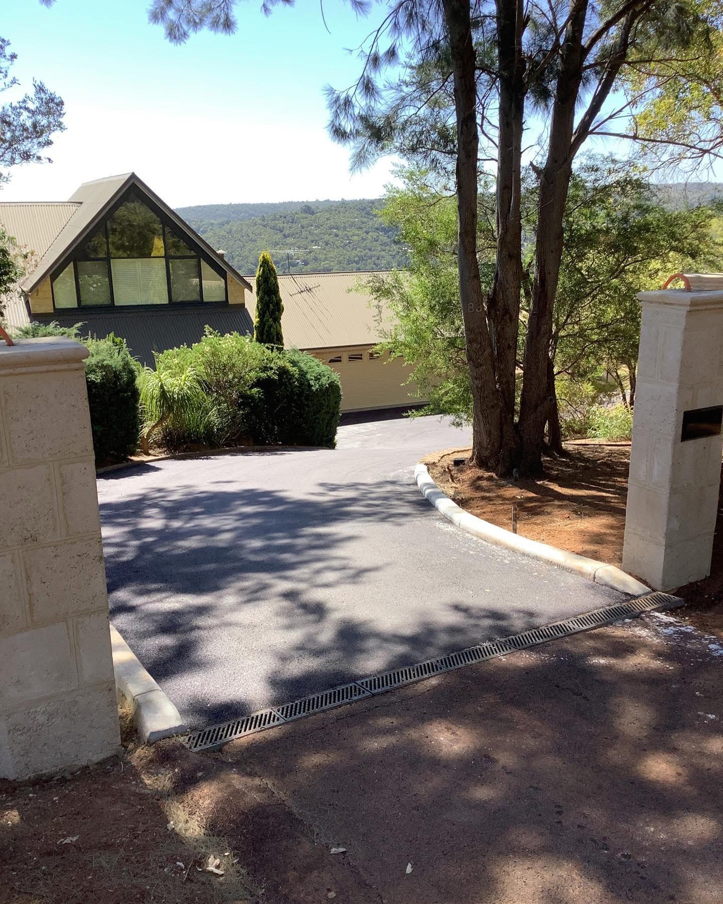 YongaCivil freshly laid asphalt residential driveway curving up to a Perth Hills home with rendered stone entry pillars and bushland surrounds