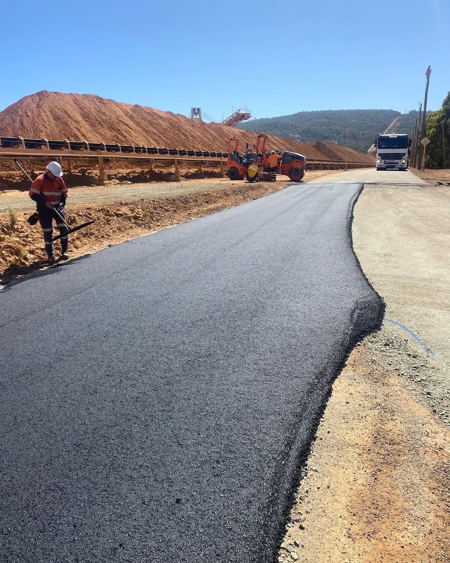 YongaCivil freshly laid asphalt haul road at a Western Australian mine site with rollers compacting the surface beside an ore stockpile