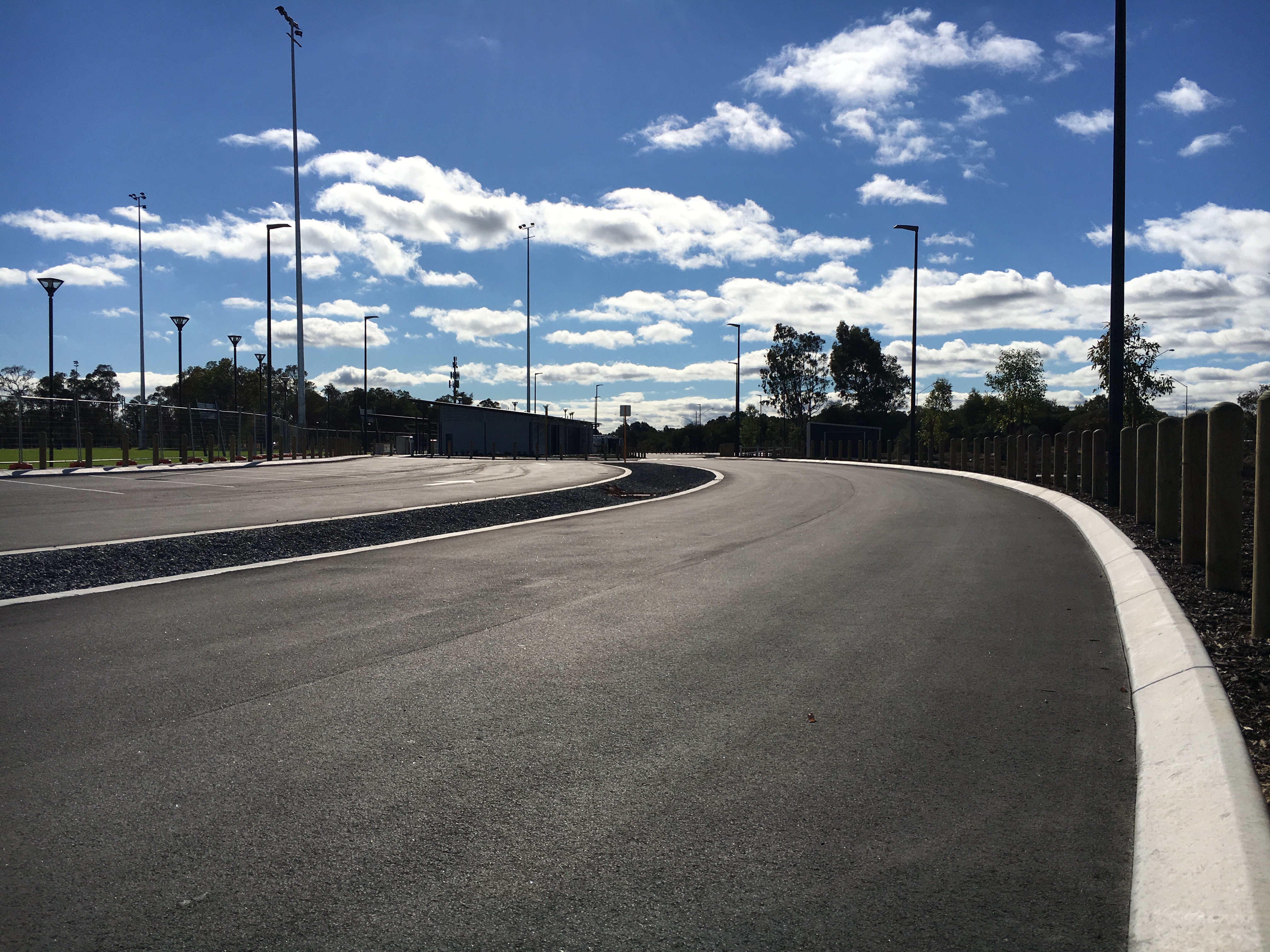 YongaCivil freshly laid asphalt access road with white concrete kerbing sweeping through a Western Australian sports complex under a blue sky