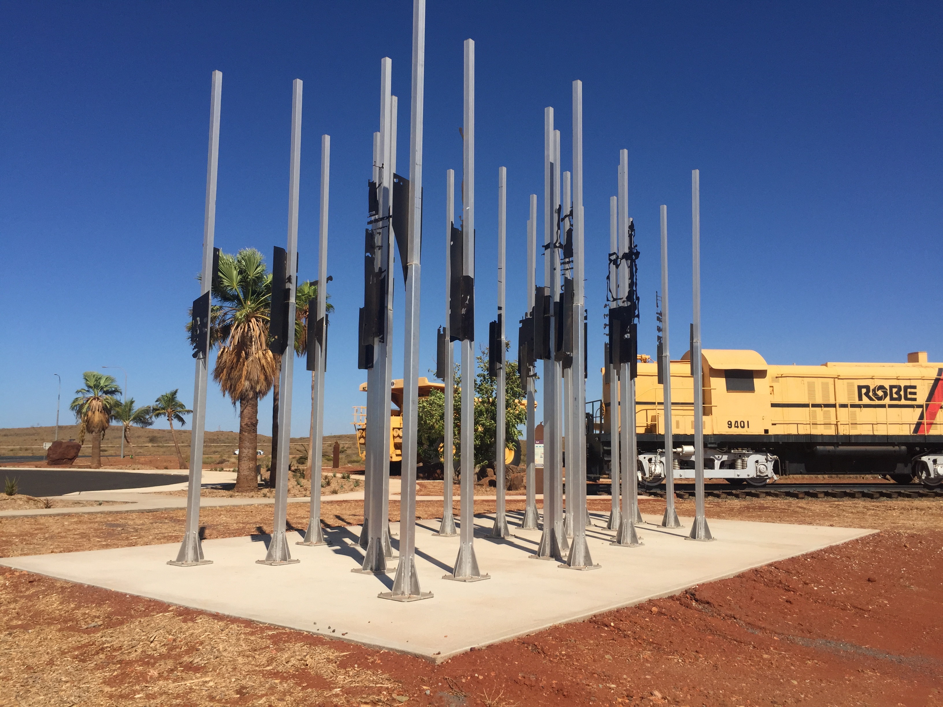 Public art installation of steel poles mounted on a poured concrete pad beside a heritage locomotive display in a regional Western Australian town plaza built by YongaCivil