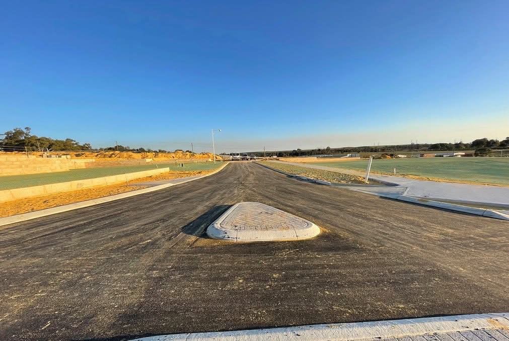 Newly constructed subdivision road with fresh asphalt, a raised concrete median island and concrete kerbing lining both edges on a YongaCivil civil works project in Western Australia