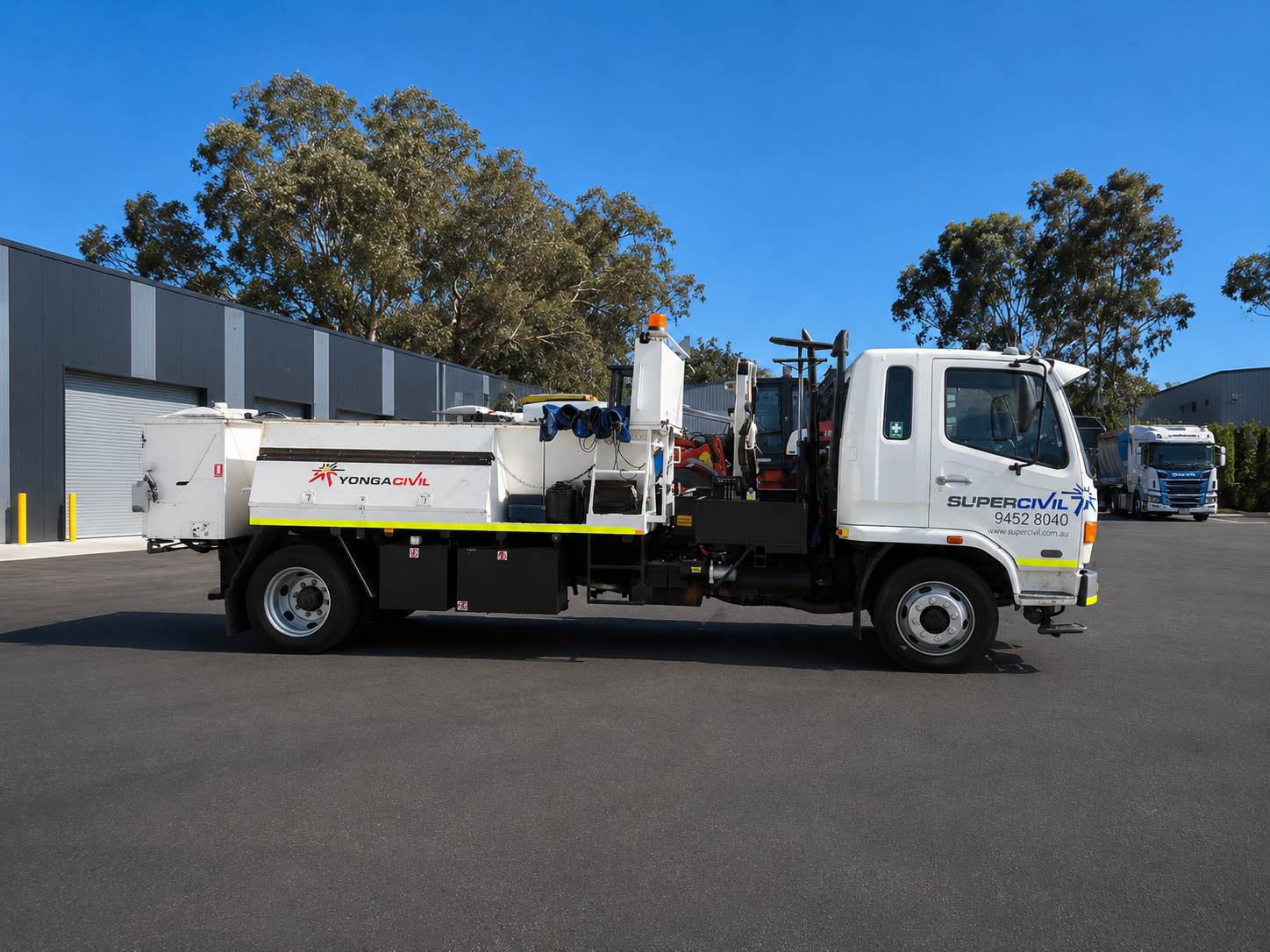 White YongaCivil Hino flocon maintenance truck fitted with road maintenance equipment, parked outside an industrial warehouse under a clear blue sky in Western Australia